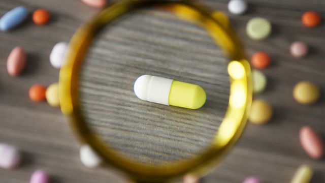 Various drugs such as antibiotics on a desk with one pill under a magnifying glass, representing drug repurposing. 